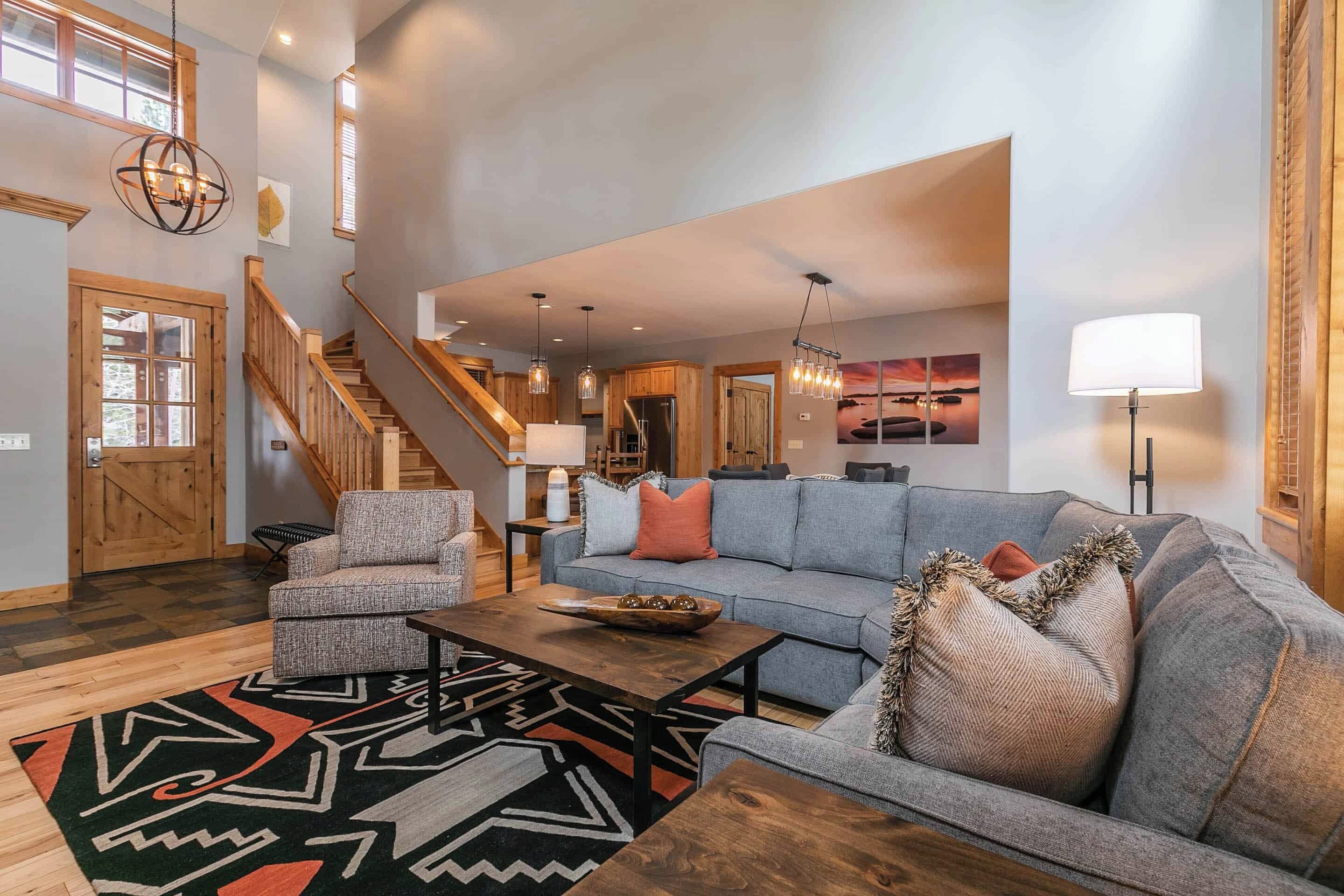 A spacious living area with a gray sofa, a wooden coffee table, and a patterned rug. A staircase with wooden railings leads to an upper level.