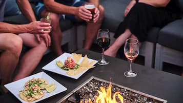 A group of people seated on a couch with a table in front of them, holding drinks and plates of food.