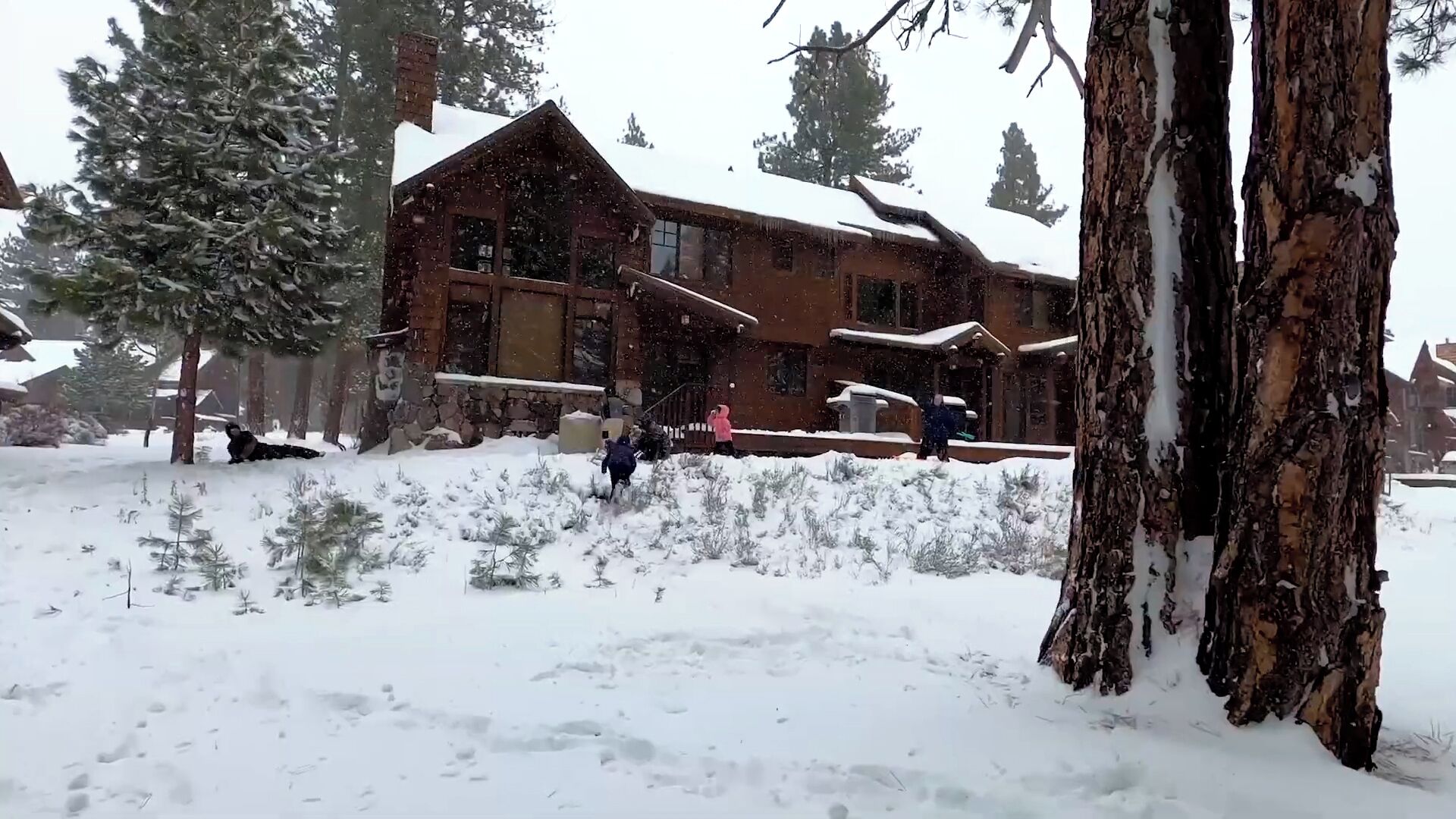 A large log cabin with a stone foundation, surrounded by snow-covered trees.