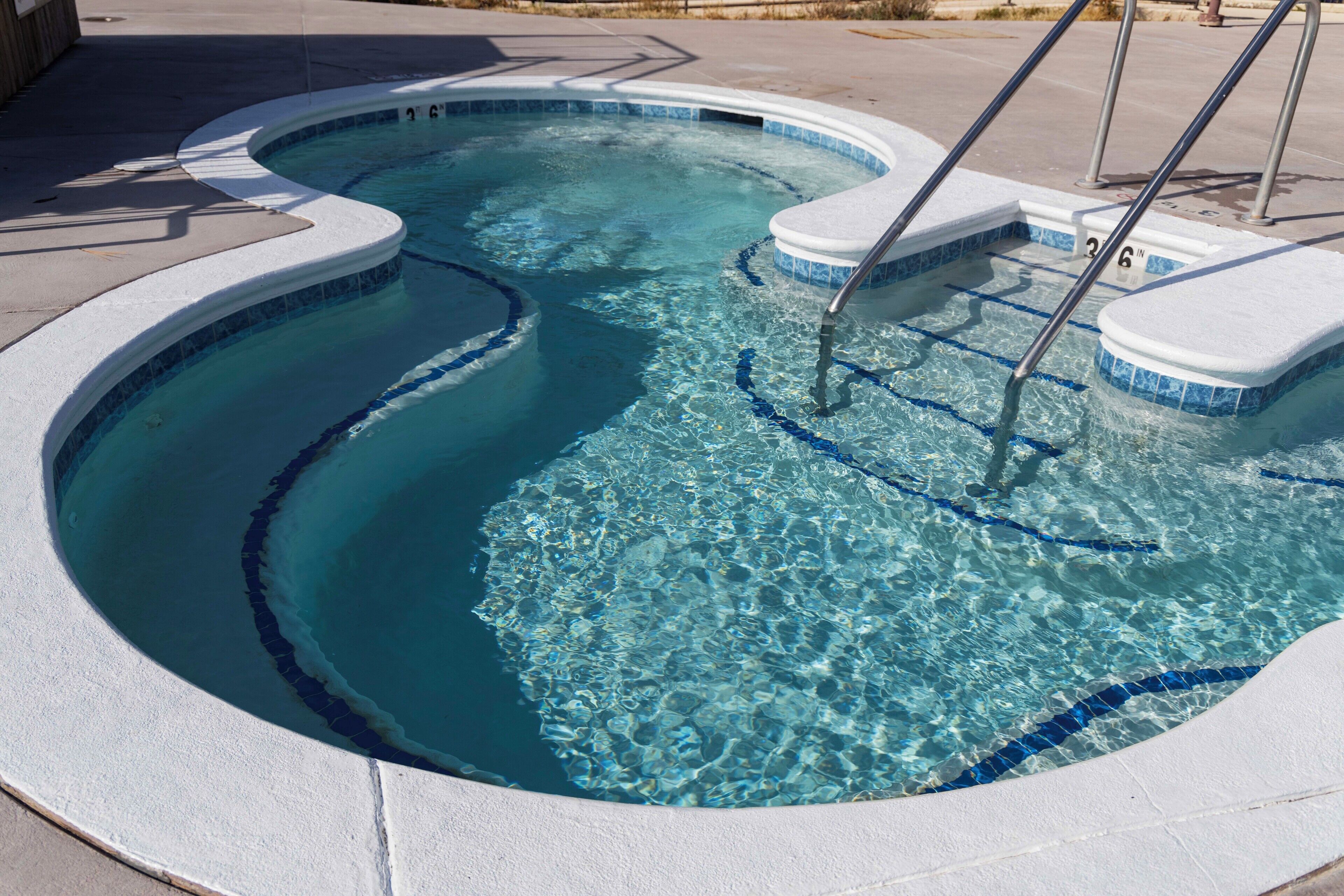 Una bañera de hidromasaje circular y transparente, con borde de azulejos y escalones metálicos para entrar.