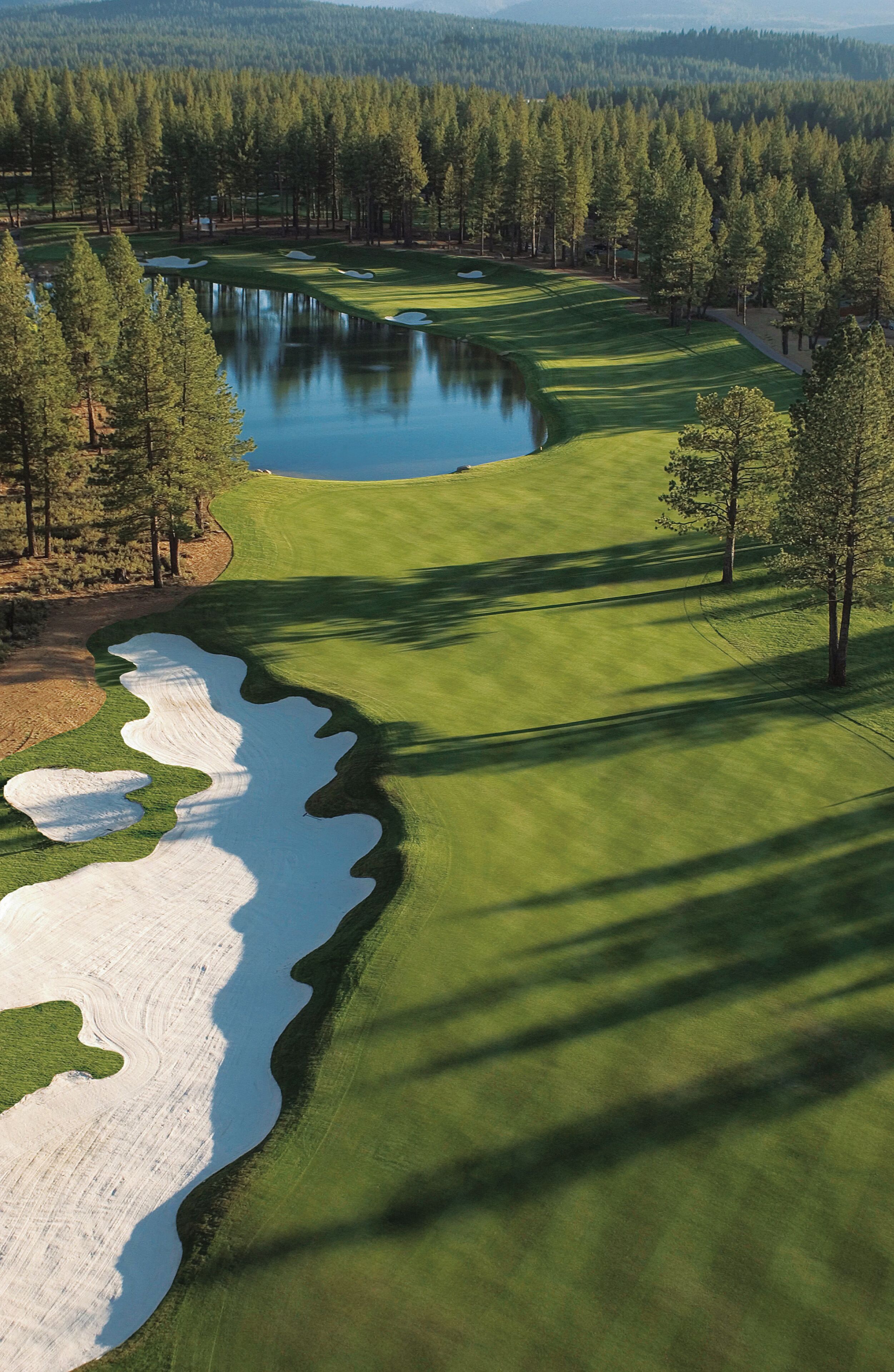 Campo de golf con búnkeres de arena, un estanque y una zona boscosa.