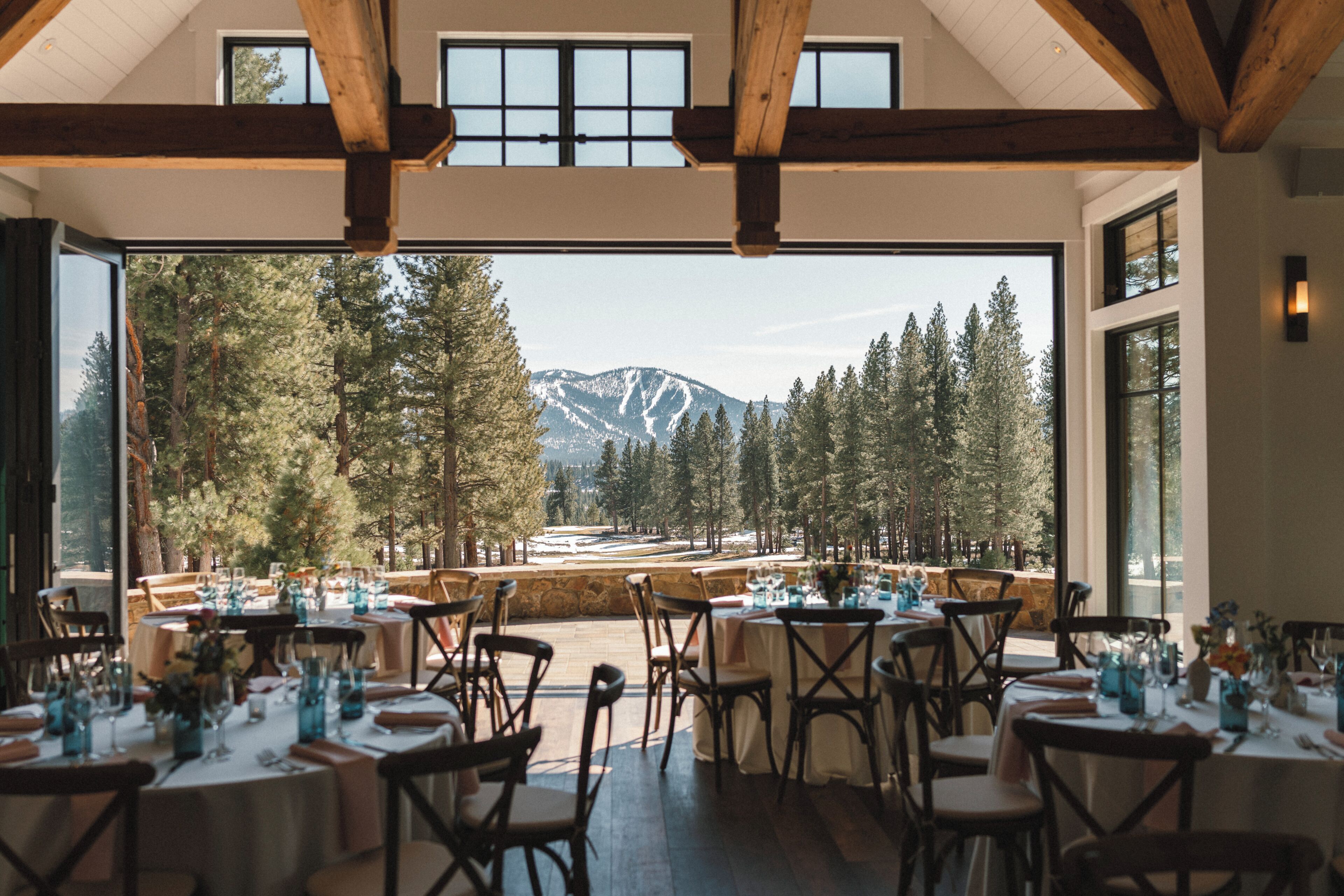 Un espace de restauration intérieur avec des tables dressées pour les clients, de grandes fenêtres offrant une vue sur une montagne enneigée et une forêt.