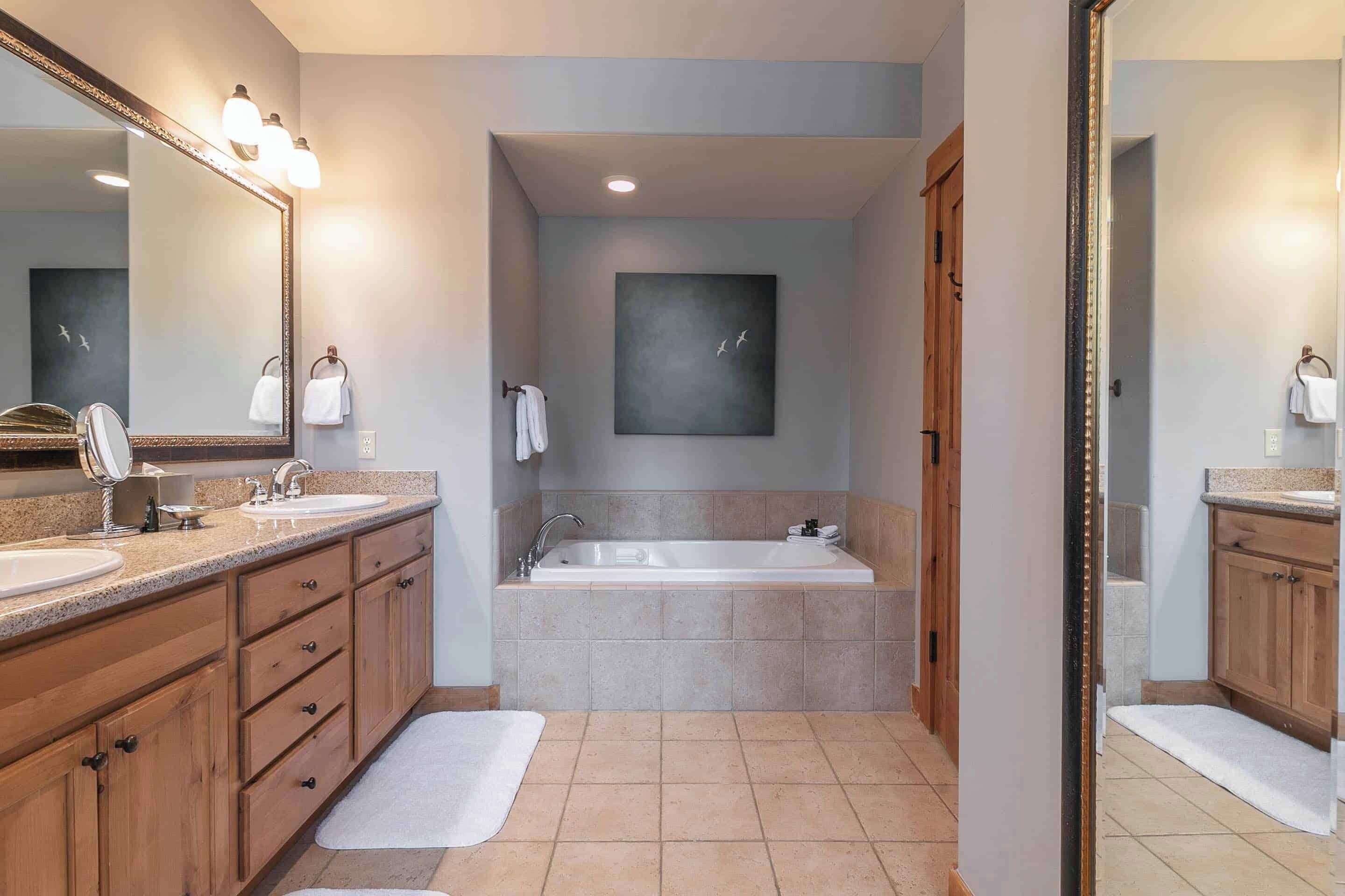 A modern bathroom with a large mirror, two sinks, a bathtub, and a towel rack.
