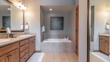 A modern bathroom with a large mirror, two sinks, a bathtub, and a towel rack.