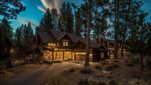 A large log cabin with multiple bedrooms, a covered porch, and a driveway leading to the entrance. - The Cottages at Old Greenwood (Truckee)