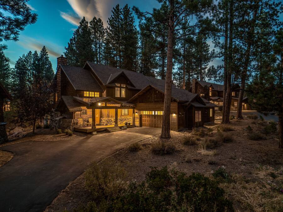 Una cabaña grande de madera con varias habitaciones, un porche cubierto y un camino de entrada.