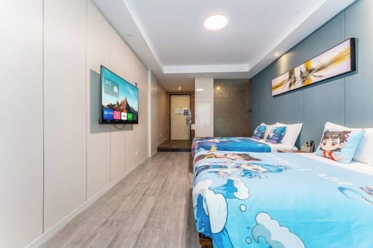 Quarto de hotel com televisão na parede, cama com roupa de cama temática de desenho animado e uma pintura acima da cama.