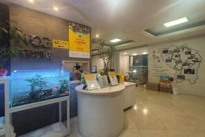 A hotel reception area with a reception desk, a fish tank, and a wall with a map and informational posters. - weige Boutique Hotel (Shaoxing)