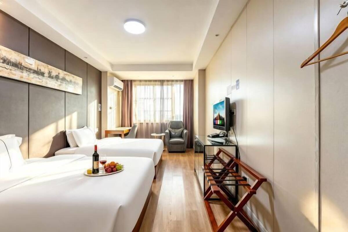 Quarto de hotel com duas camas, uma escrivaninha, uma televisão e um quadro na parede.