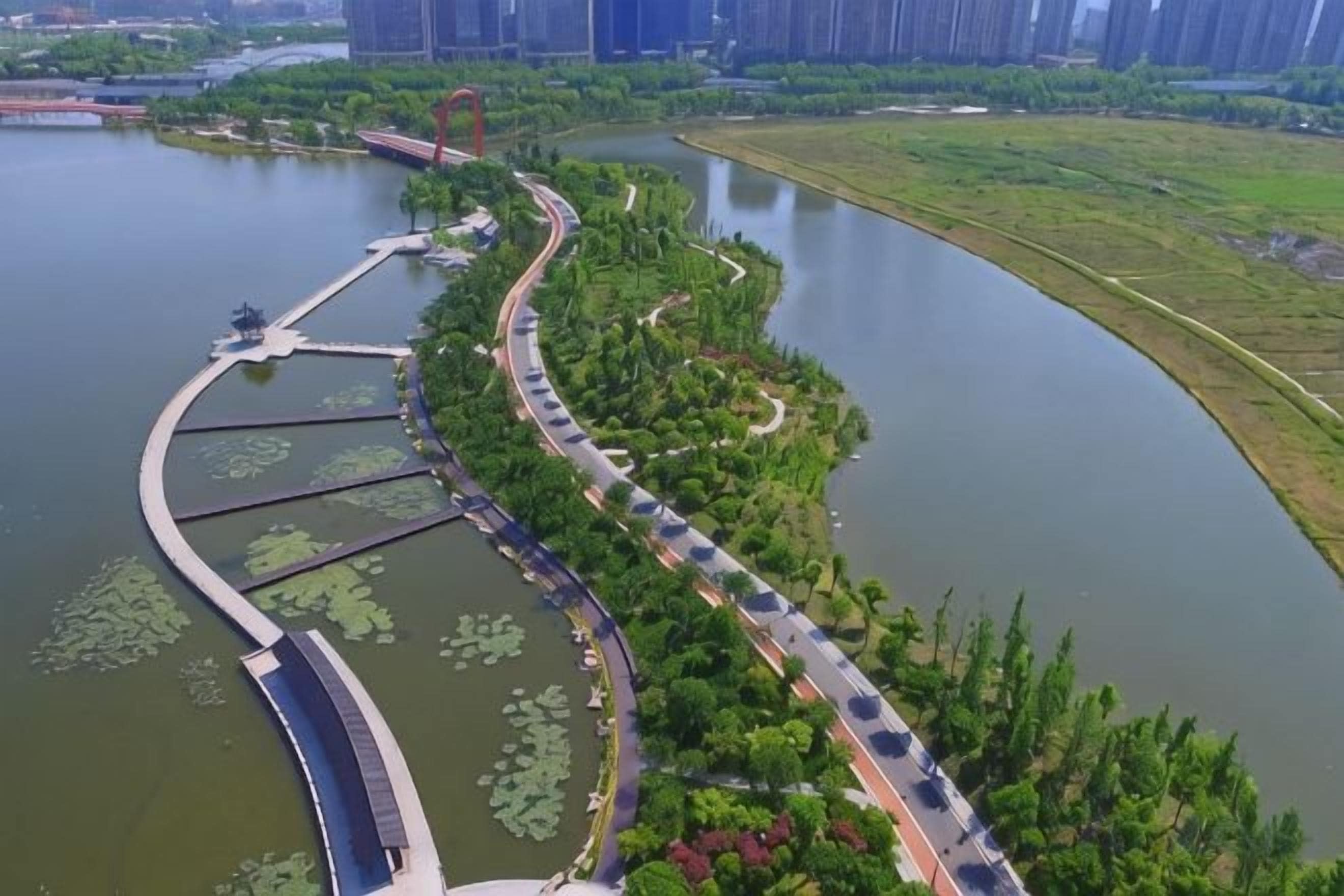 Un parque junto al río con senderos para caminar, un puente y una pequeña isla con nenúfares.