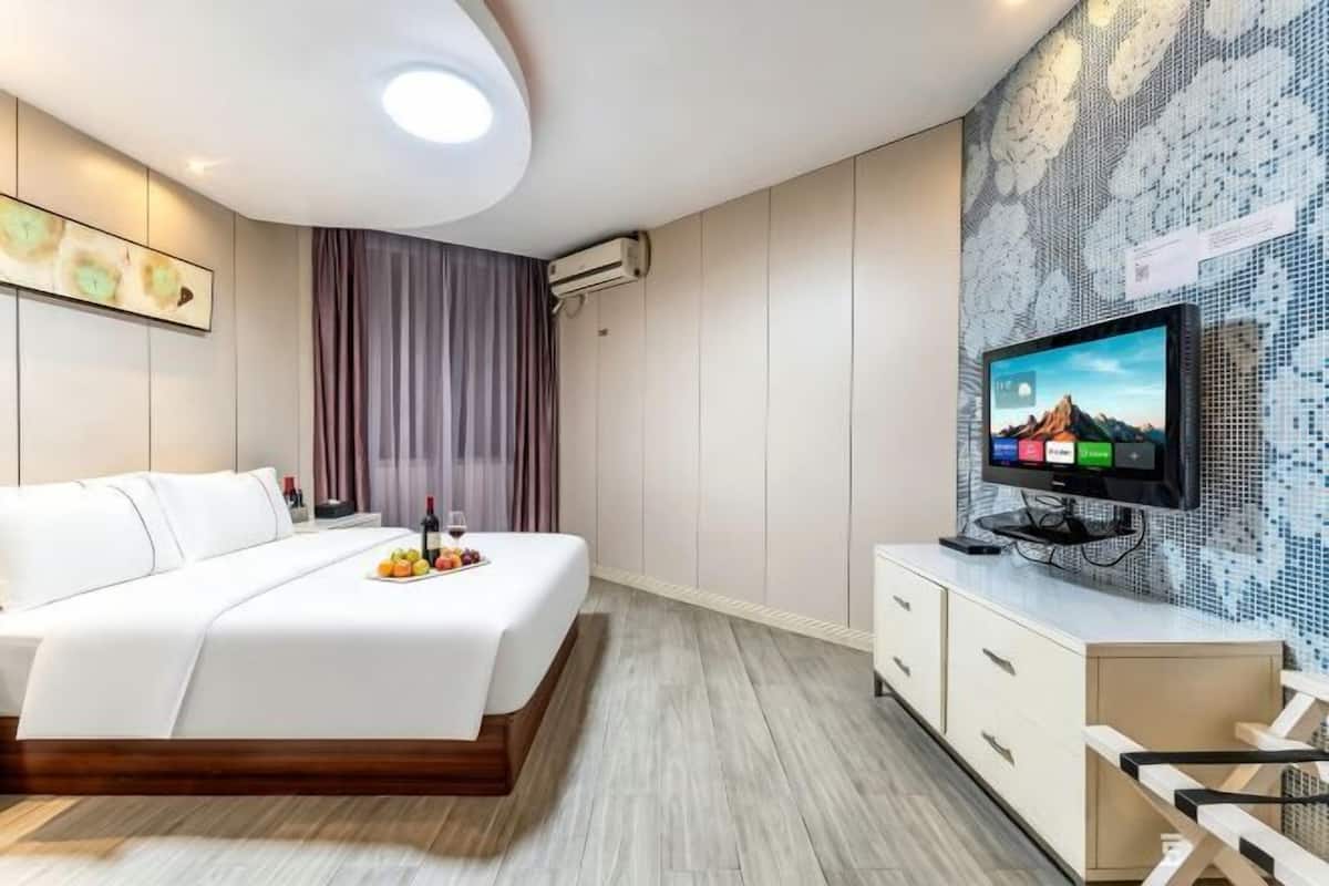 Quarto de hotel moderno com cama, televisão, frigobar e parede com padrão em mosaico.