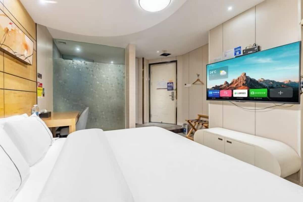 Quarto de hotel moderno com uma cama, uma escrivaninha, uma televisão e área de chuveiro.