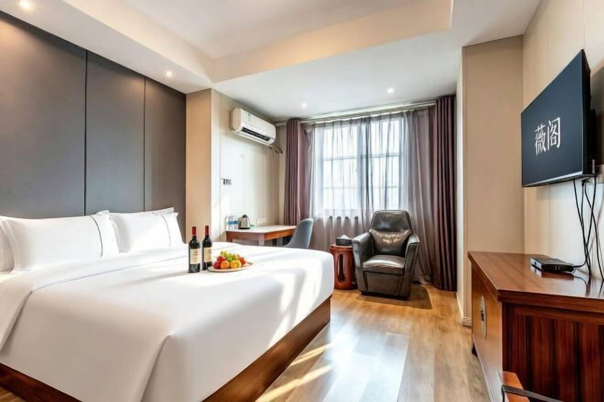 Quarto de hotel com uma cama grande, uma escrivaninha, uma cadeira, uma televisão e um aparelho de ar condicionado.