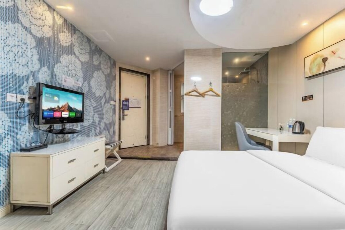 A modern hotel room with a large bed, a desk, a television, and a shower area.