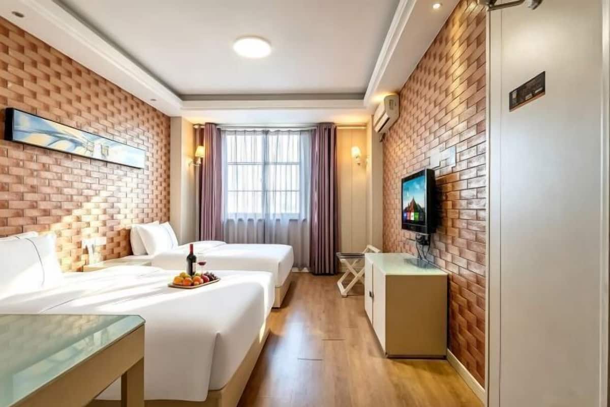 Quarto de hotel com duas camas, televisão, parede de tijolos e janela com cortinas.