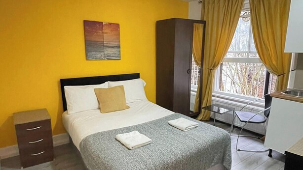 A hotel room with a bed, a small desk, a chair, a wardrobe, and a window with curtains. - Studio Sleeps 2 With Internet Access (London)