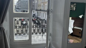 A room with a view of a street, a bed with a nightstand, and a green wall. - Apartment Sleeps 2 With Balcony (London)