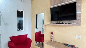 A modern living room with a red chair, a mounted TV, a mirror, and a shelf with toiletries. - Pousada Oásis do Sertão (Euclides Da Cunha)