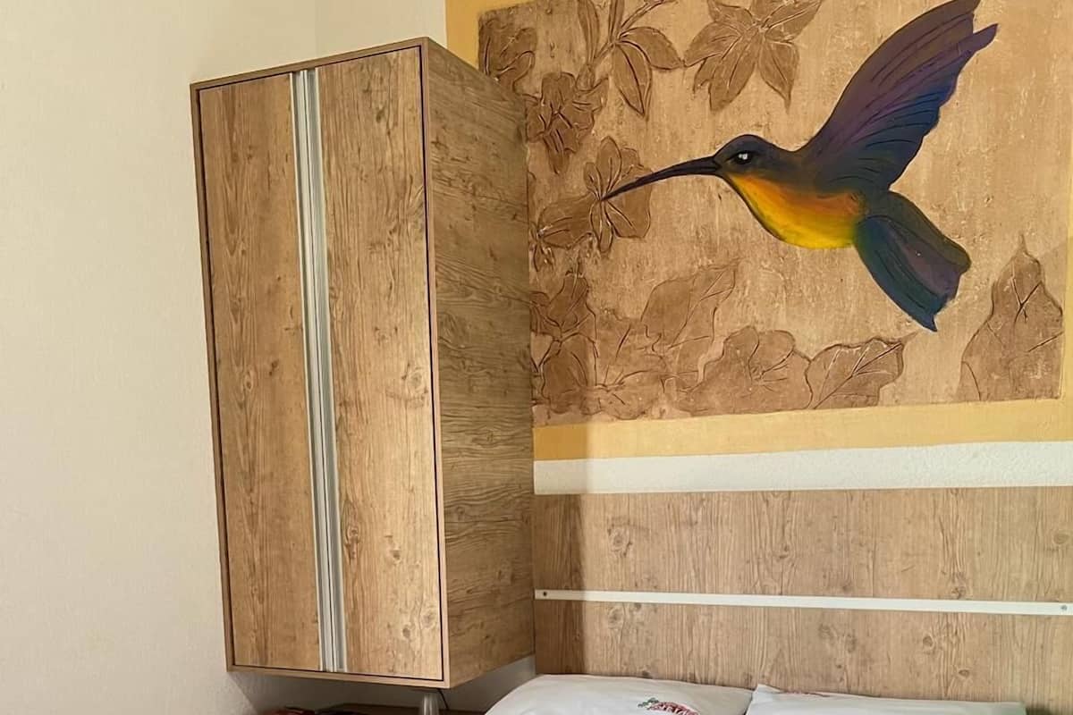 Ein Hotelzimmer mit einem Bett, einem Holzschrank und einem Wandbild eines Kolibris.