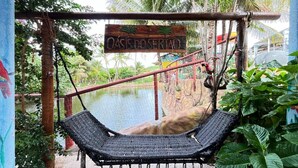 A hammock swing with a sign reading "OASIS DOSERIAO" in a tropical setting with a water body and lush greenery. - Pousada Oásis do Sertão (Euclides Da Cunha)