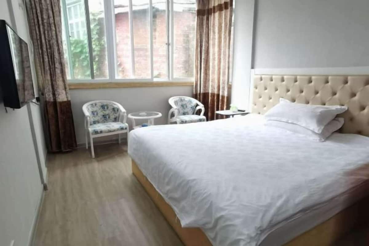 Hotellihuone, jossa on sänky, kaksi tuolia, pieni pöytä ja televisio.