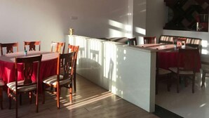 Un comedor con mesas y sillas redondas, una isla central con encimera blanca y vistas al exterior a través de una ventana.