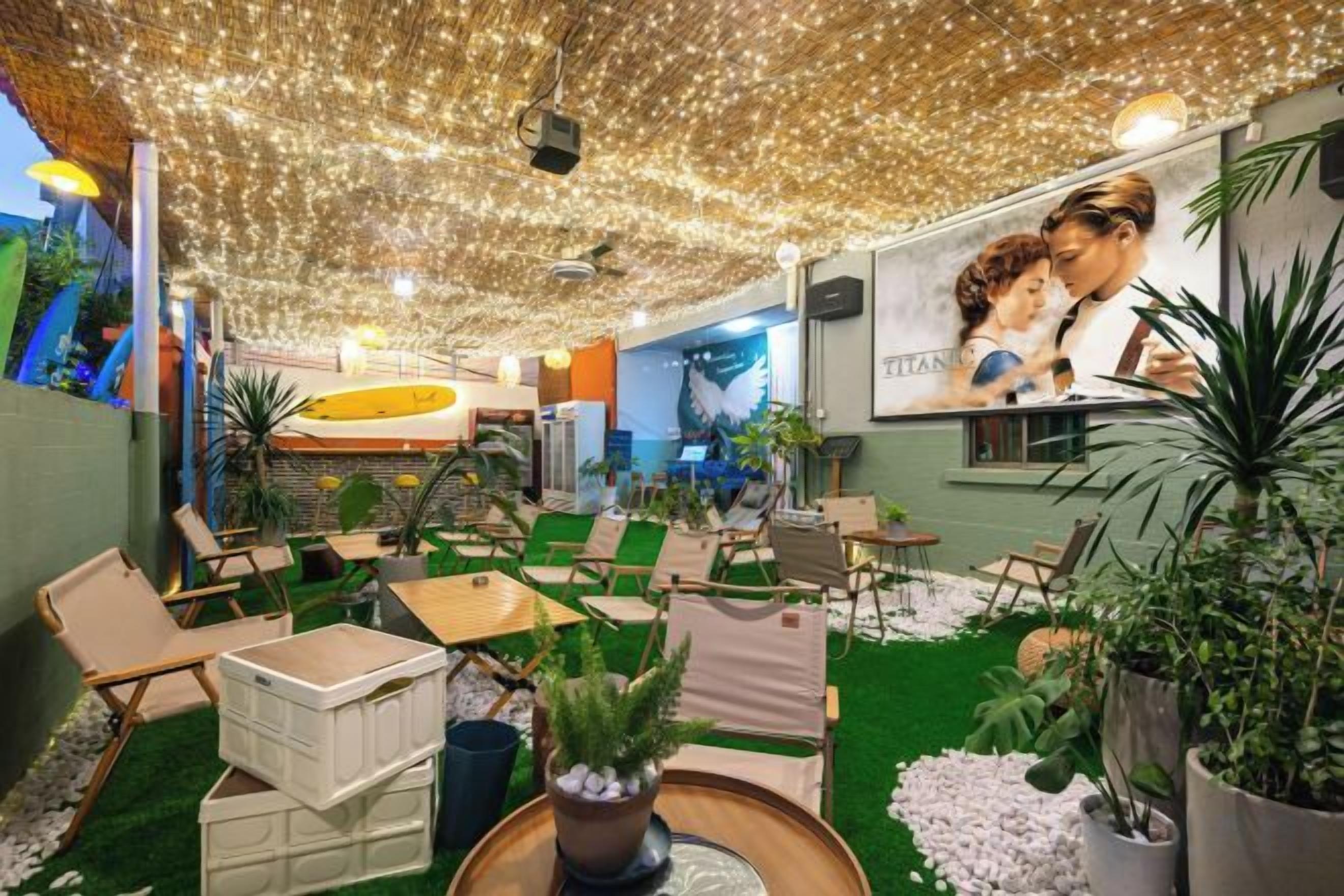 A cozy indoor seating area with green artificial turf, potted plants, and a ceiling adorned with string lights.