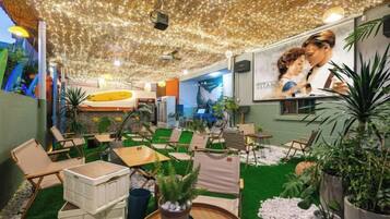 A cozy indoor seating area with green artificial turf, potted plants, and a ceiling adorned with string lights.