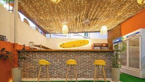 A bar area with a brick wall, a surfboard decoration, and three yellow bar stools. - Shenzhen Xinghai Xiaoye Inn (Shenzhen)