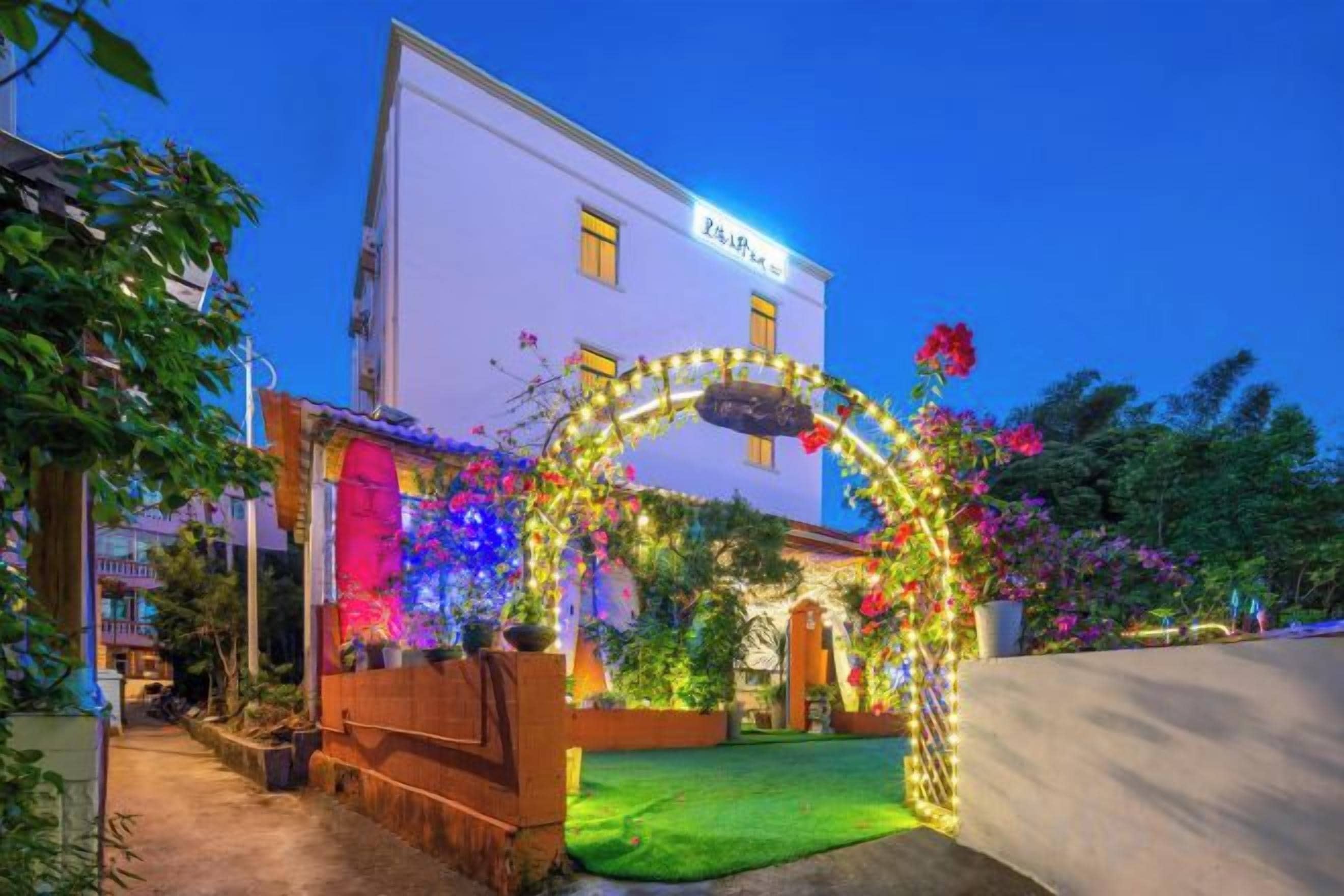 Un bâtiment à la façade blanche, doté d’une entrée en arc de cercle et d’un espace jardin agrémenté de plantes et de fleurs.