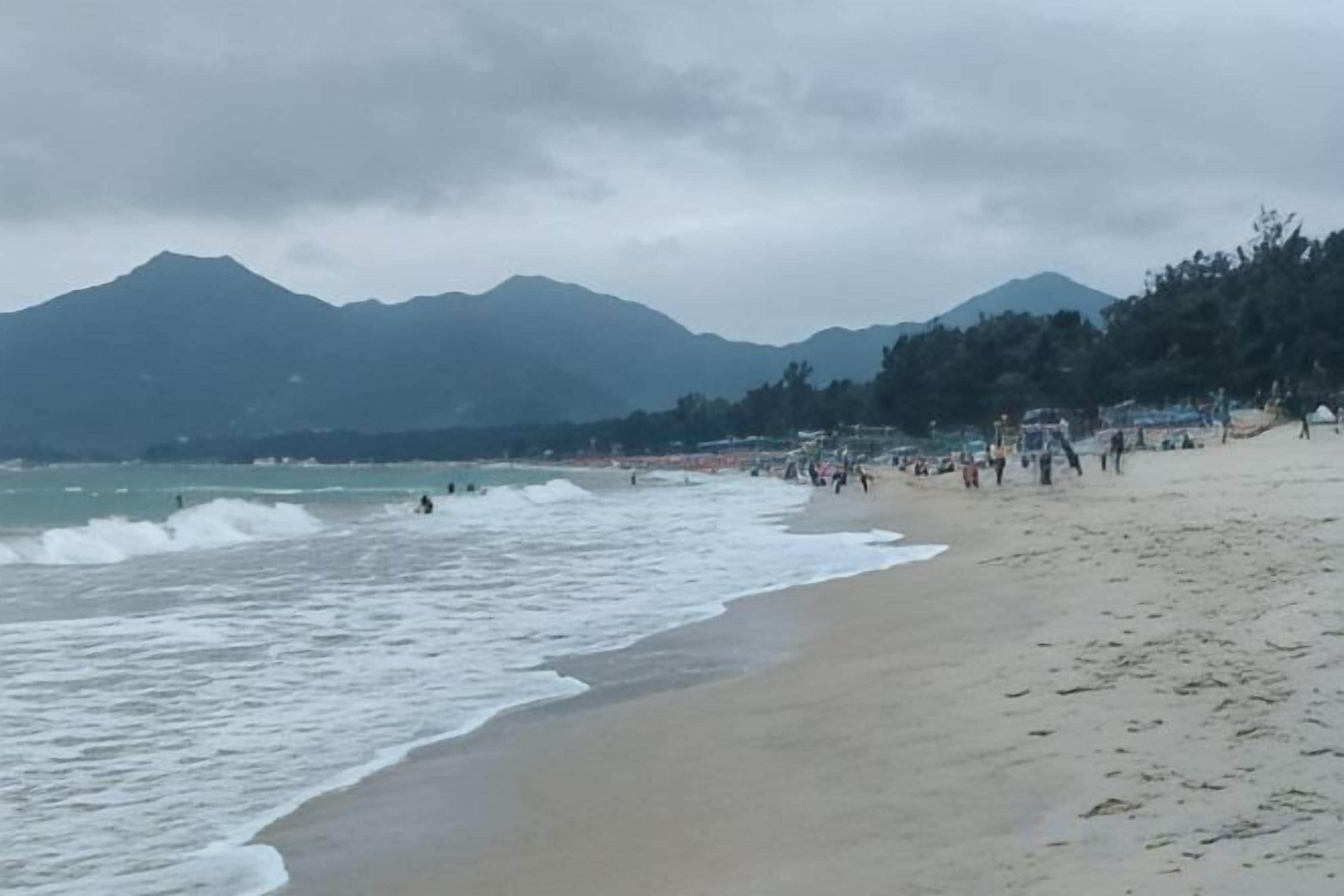 Ein Strand mit Wellen, einer Menschenmenge und Bergen im Hintergrund.