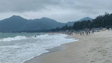 Ein Strand mit Wellen, einer Menschenmenge und Bergen im Hintergrund.