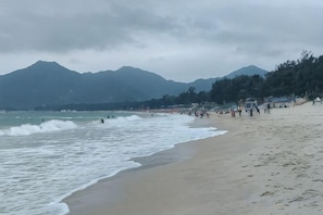 A beach with waves, a crowd, and mountains in the background. - Shenzhen Xinghai Xiaoye Inn (Shenzhen)
