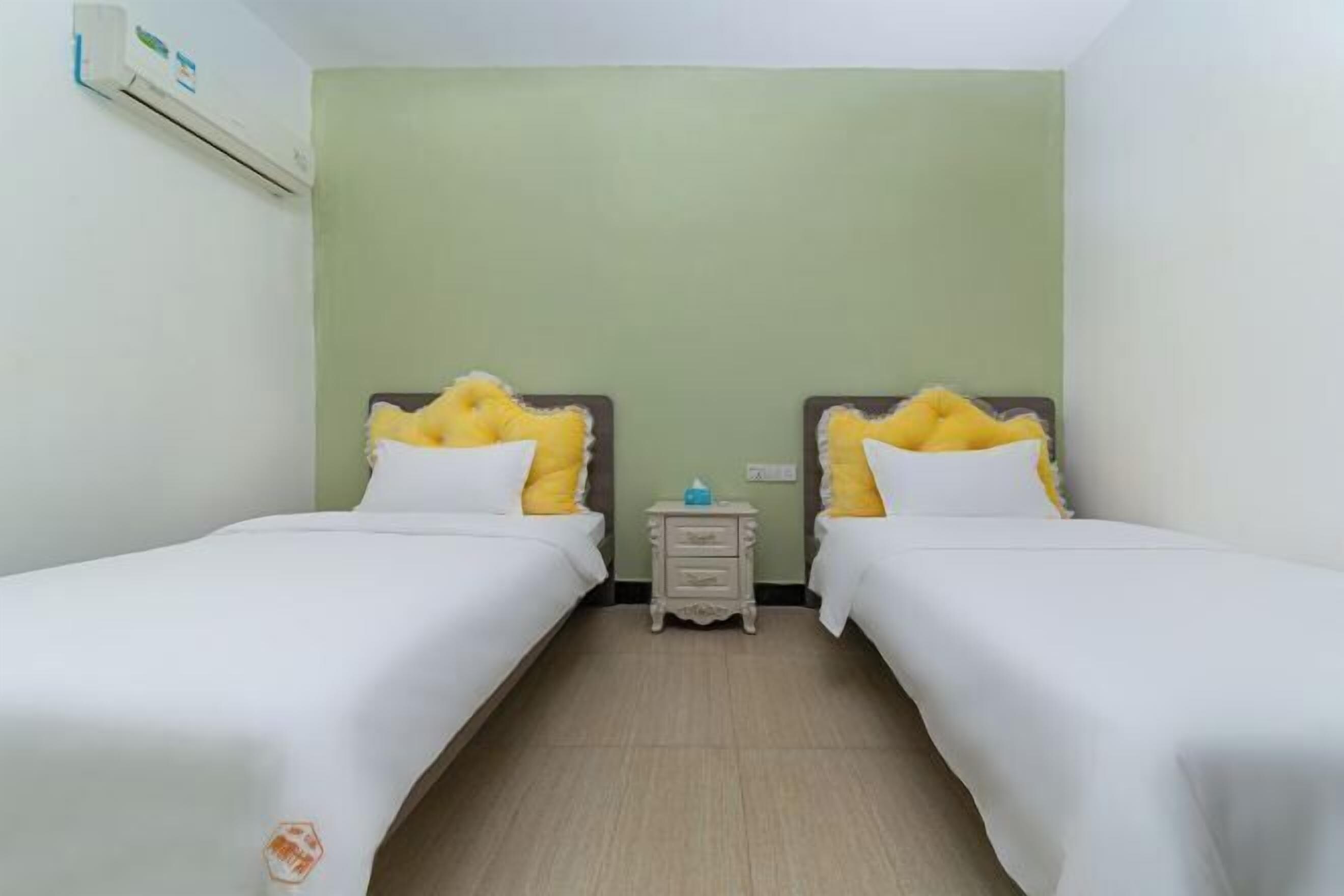 A hotel room with two single beds, a small bedside table, and a wall-mounted air conditioner.