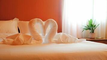 Una cama con un arreglo de almohadas en forma de corazón y una planta en maceta sobre una mesita de noche.