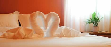 A bed with a heart-shaped pillow arrangement and a potted plant on a nightstand.