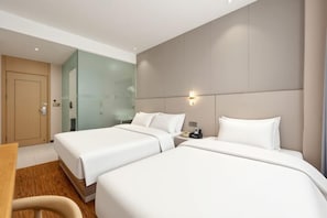 A hotel room with two beds, a wooden desk, and a glass-enclosed bathroom. - Hengsheng Hotel (Fuzhou Railway Station North Square) (Fuzhou)
