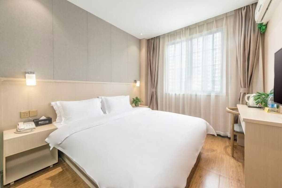 A hotel room with a large bed, bedside tables, a desk, and a window with curtains.