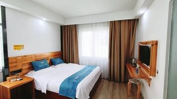 A hotel room with a bed, wooden headboard, a small wooden table, a television, and a window with curtains.