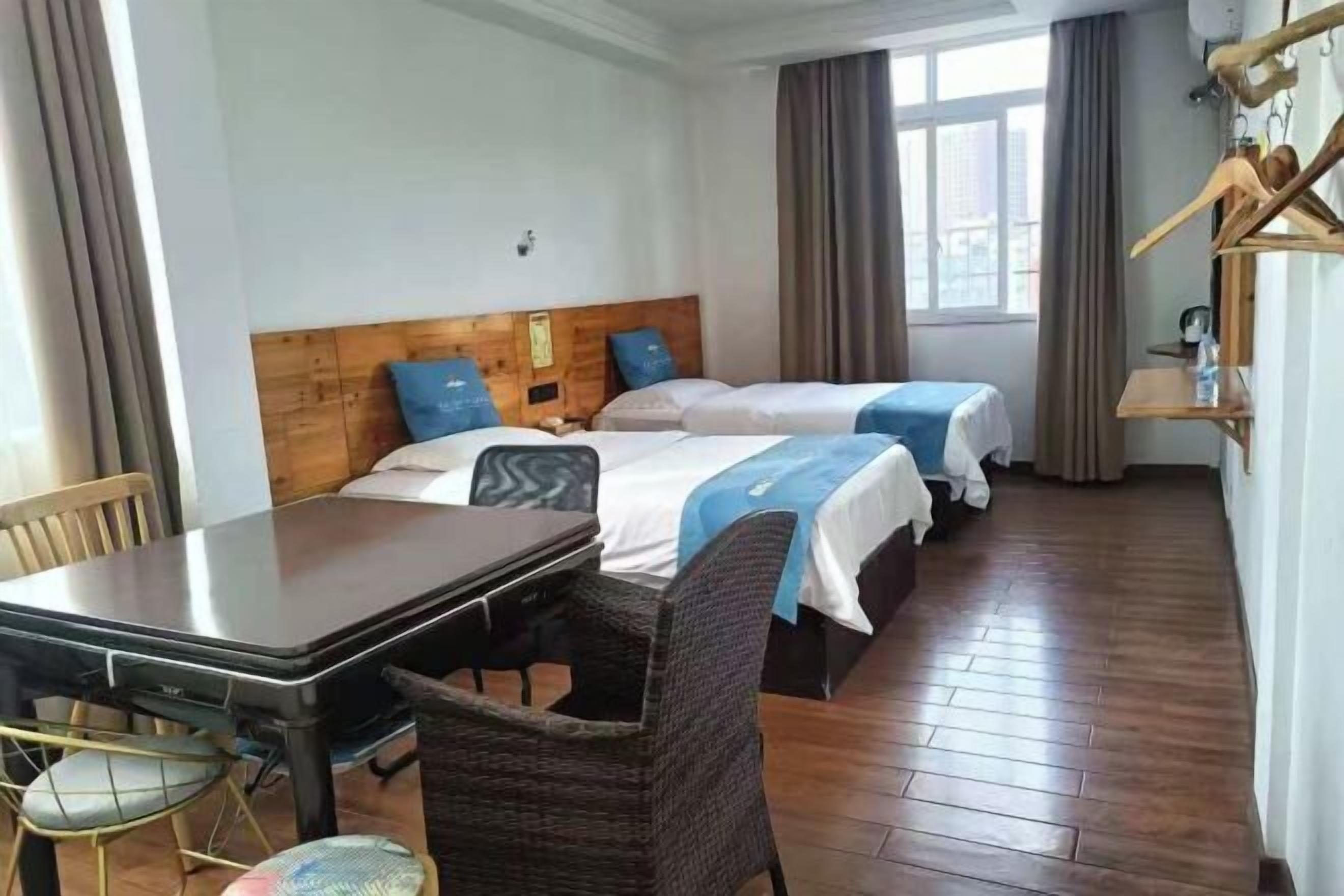 A hotel room with two beds, a wooden headboard, a dining table with chairs, and a window with curtains.