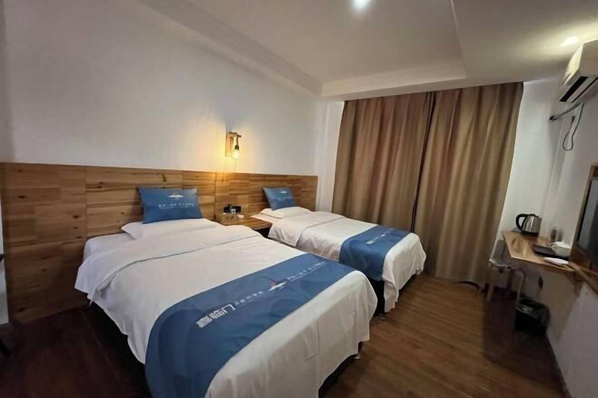 Hotellihuone, jossa on kaksi sänkyä, puinen pääty, yöpöytä, työpöytä tuolilla ja ikkuna, jossa on verhot.