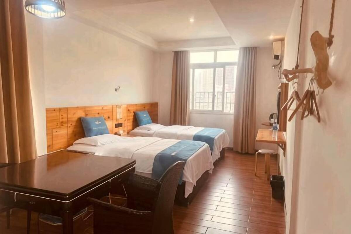 Hotellihuone, jossa on kaksi sänkyä, puinen työpöytä, tuoli, ikkuna ja seinään kiinnitetty valaisin.