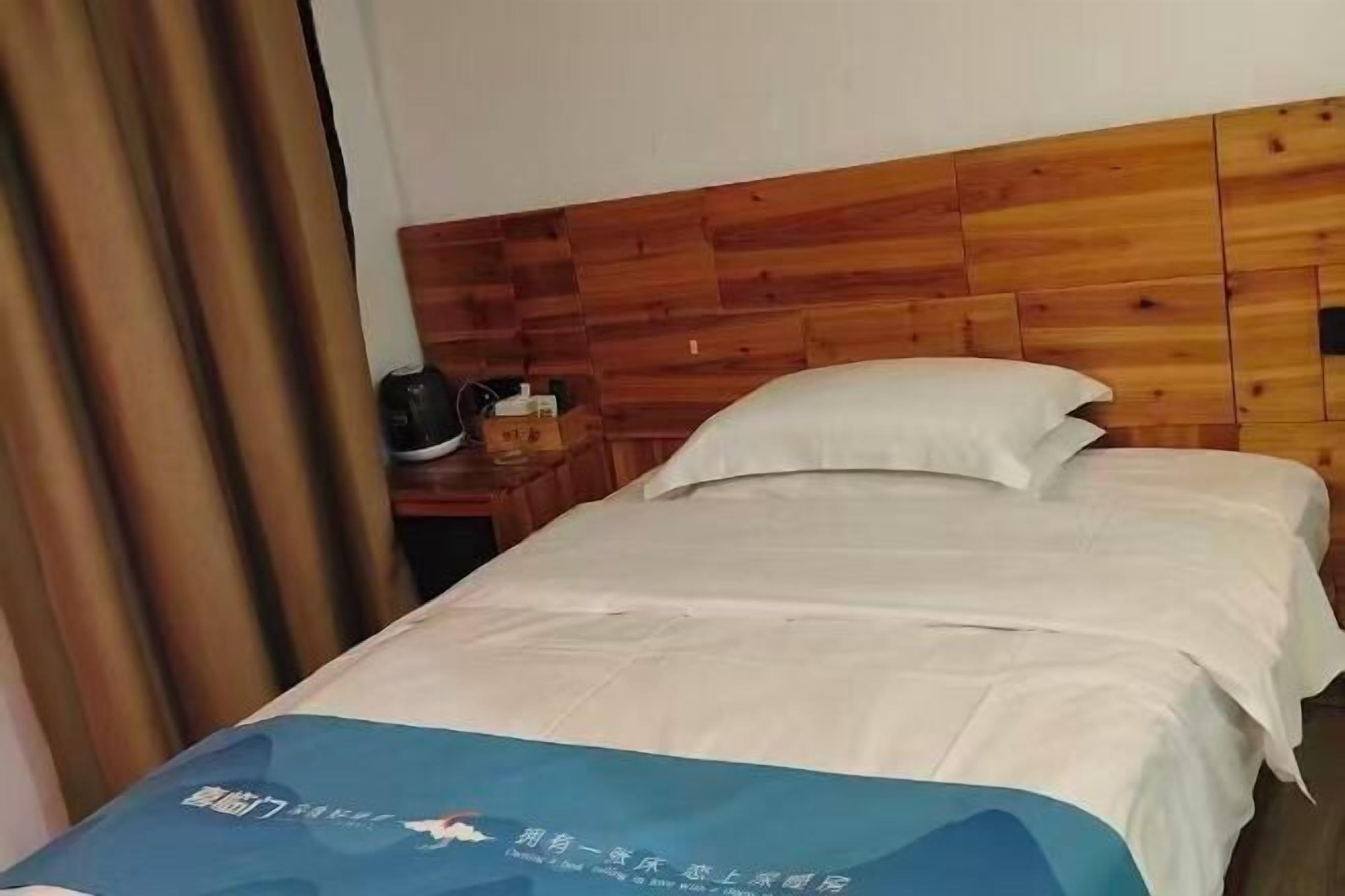 Una habitación de hotel con cabecera de madera, cama con ropa de cama blanca y manta azul con texto.