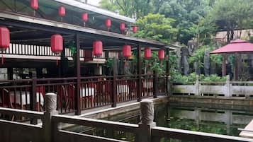 Un edificio de estilo tradicional con un paseo techado, un estanque y faroles rojos.