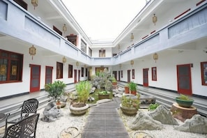 Un patio con un sendero central, plantas en macetas y puertas rojas tradicionales.