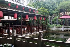Un pavillon traditionnel avec une balustrade en bois, un étang et des lanternes rouges.