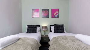 Une chambre double avec deux lits, une table de chevet, une lampe et trois œuvres d’art accrochées au mur.