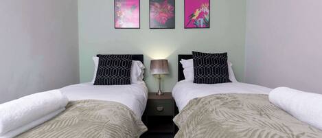 Une chambre double avec deux lits, une table de chevet, une lampe et trois œuvres d’art accrochées au mur.