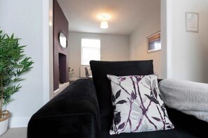A living room with a black sofa, a patterned pillow, and a grey blanket.