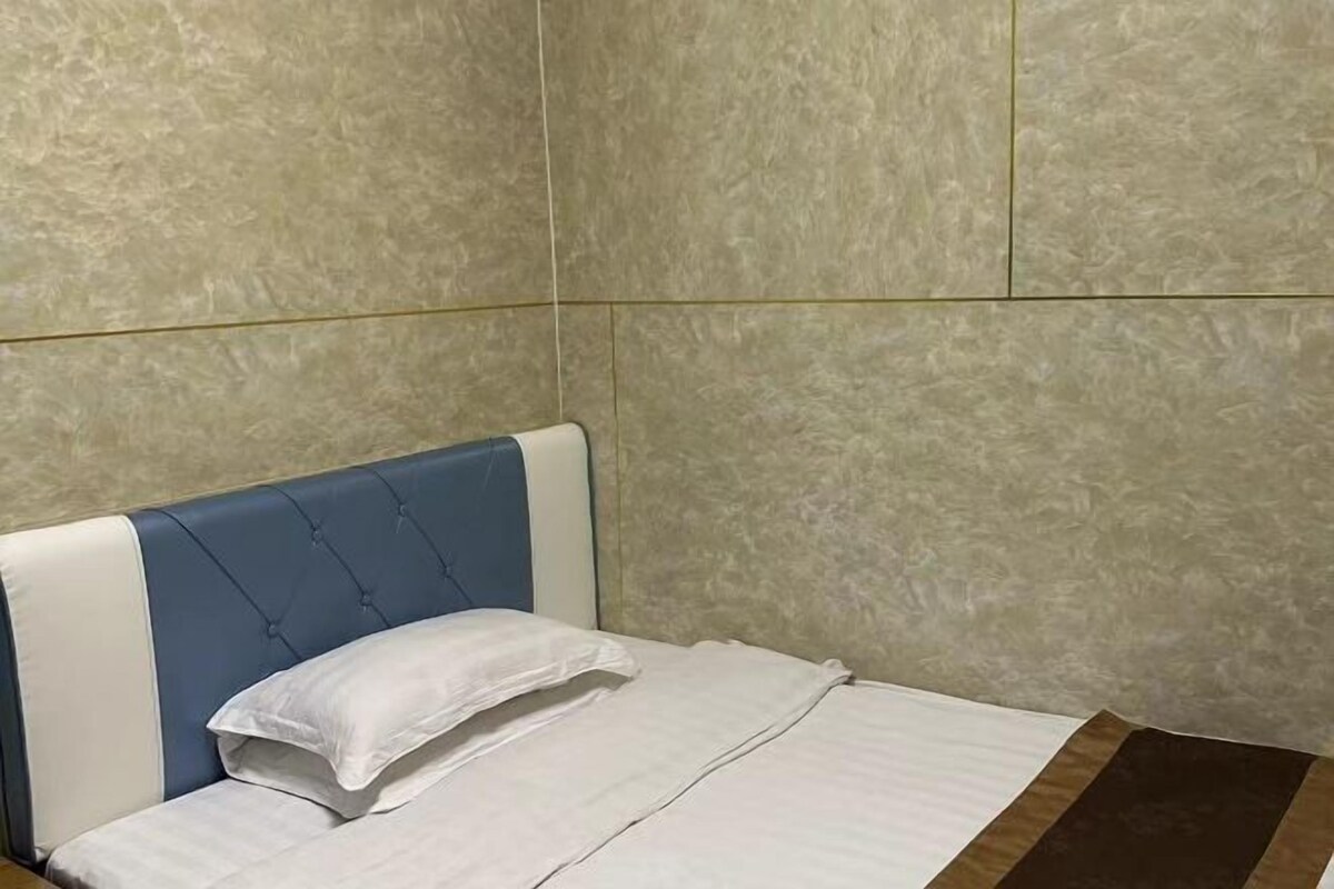 Cama com cabeceira e travesseiro brancos, em frente a uma parede texturizada.